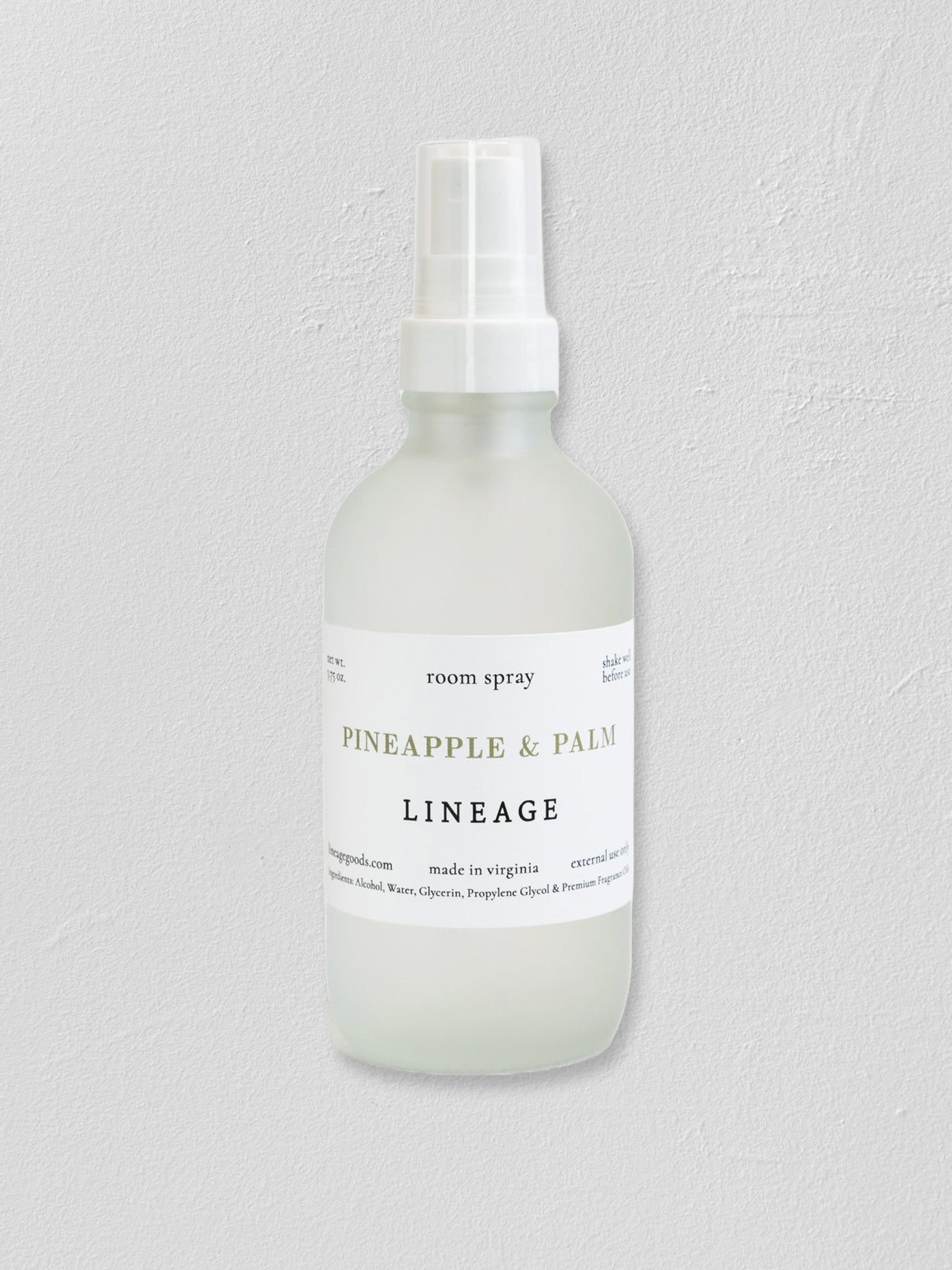 A frosted glass room spray bottle with a white spray top and a white label reading 'PINEAPPLE & PALM LINEAGE' on a light gray textured background.